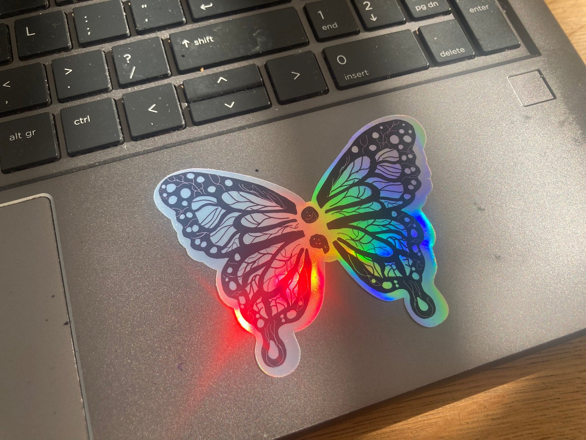Holographic semicolon butterfly sticker shown as laptop sticker, handmade by NeurodiverseTea