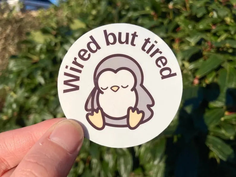 "Wired but tired" sleepy penguin sticker with text, handmade by small business Neurodiversetea